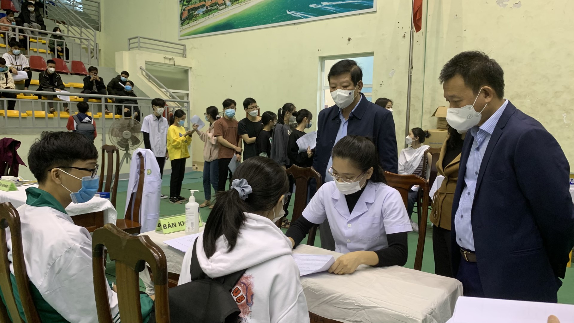 Lãnh đạo ngành Y tế giám sát điểm tiêm vắc xin phòng Covid 19 cho các em học sinh. Custom